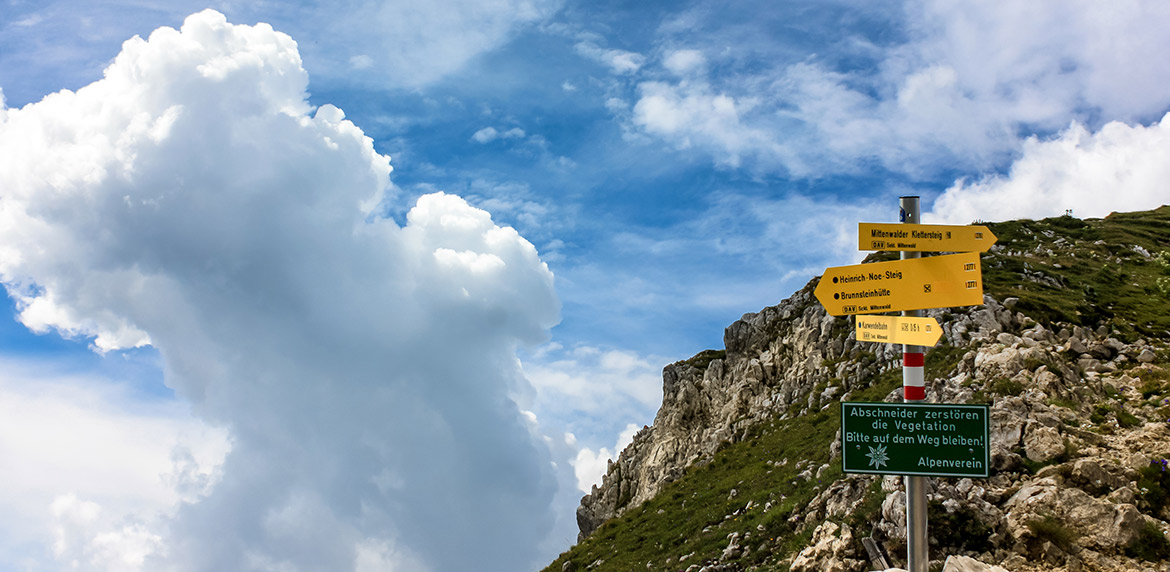 Das Bild zeigt eine Berglandschaft mit Wegweisern und einem Hinweisschild vom Alpenverein, dass man die Wege bitte nicht verlassen soll.