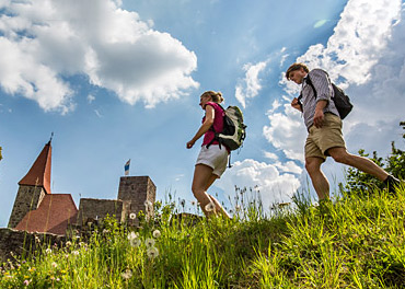 Das Bild zeigt 2 Wanderer auf einer Wiese vor einer Burg